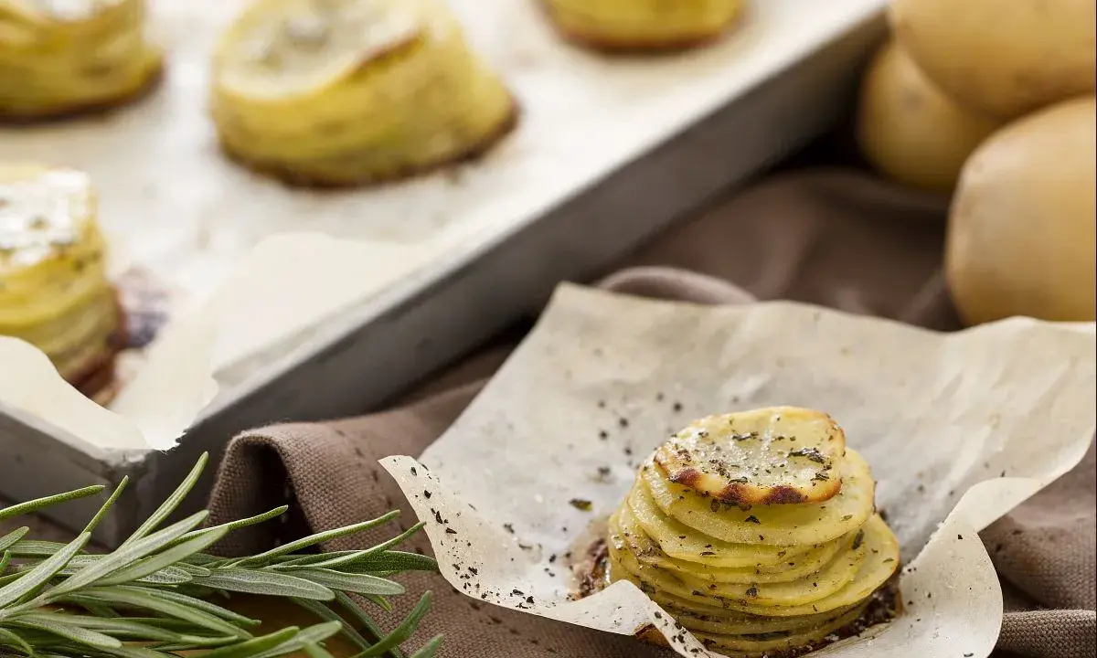 Tourte de pommes de terre fines et dorées, assaisonnée d'herbes, sur du papier sulfurisé.