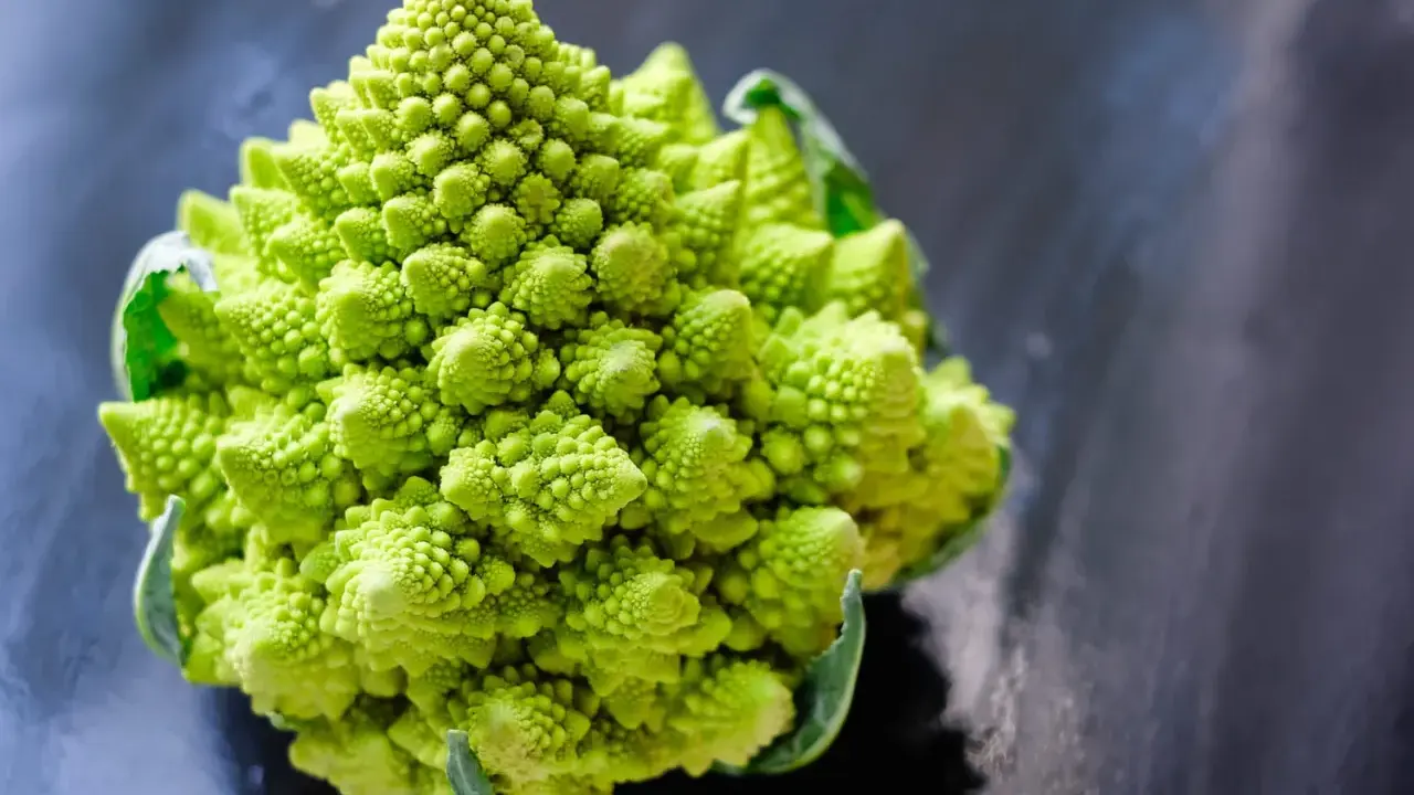 Un chou romanesco d'un vert éclatant, aux spirales parfaites, se dresse sur un fond sombre et texturé.