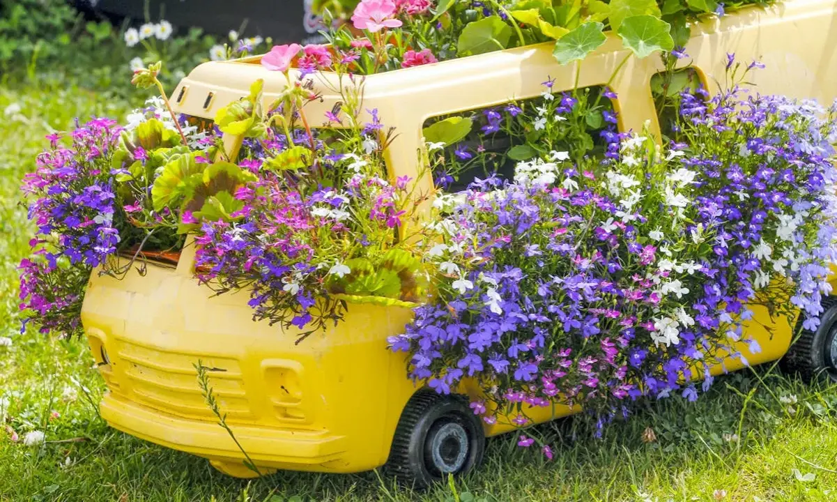 Un bus jaune transformé en jardinière déborde de magnifiques fleurs d'été aux teintes violettes, roses et blanches.