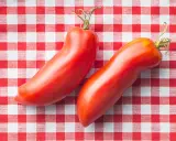 Deux tomates cornues des Andes, rouges et allongées, reposent sur une nappe à carreaux rouges et blancs.
