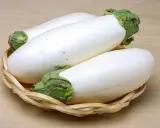 Trois aubergines blanches, d'une blancheur immaculée, reposent dans un panier en osier tressé sur un fond en bois clair.