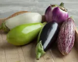 Variétés d'aubergines photos : une aubergine blanche, une verte, une noire, une violette ronde et une tigrée sur un plateau en bois.