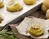 Tourte de pommes de terre fines et dorées, assaisonnée d'herbes, sur du papier sulfurisé.