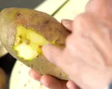 Une main touche une pomme de terre verte, révélant sa chair jaune vif sous la peau.
