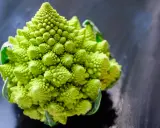 Un chou romanesco d'un vert éclatant, aux spirales parfaites, se dresse sur un fond sombre et texturé.