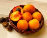 Un panier de fruits orangés, dont un coupé révélant son noyau abricot. Quelques noyaux sont dispersés à côté.