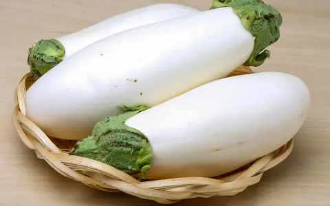 Trois aubergines blanches, d'une blancheur immaculée, reposent dans un panier en osier tressé sur un fond en bois clair.