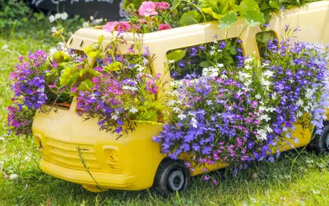 Un bus jaune transformé en jardinière déborde de magnifiques fleurs d'été aux teintes violettes, roses et blanches.