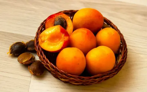 Un panier de fruits orangés, dont un coupé révélant son noyau abricot. Quelques noyaux sont dispersés à côté.