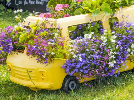 Un bus jaune transformé en jardinière déborde de magnifiques fleurs d'été aux teintes violettes, roses et blanches.