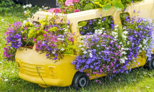 Un bus jaune transformé en jardinière déborde de magnifiques fleurs d'été aux teintes violettes, roses et blanches.